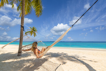 Fototapeta na wymiar Best summer travel vacation. Happy traveler bikini woman relax in hammock on sunny beach coconut palms. Leisure carefree tropical paradise sky coast seashore. Wellbeing island recreational wallpaper