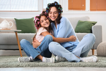 Little girl and her mother with hair curlers hugging at home