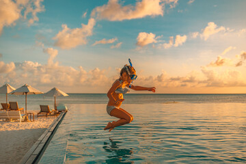 Amazing sunset sea sky with joyful girl in snorkel gear jumping into pool. Tropical resort beach...