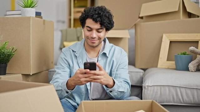 Young latin man packing cardboard box make photo by smartphone to picture at new home