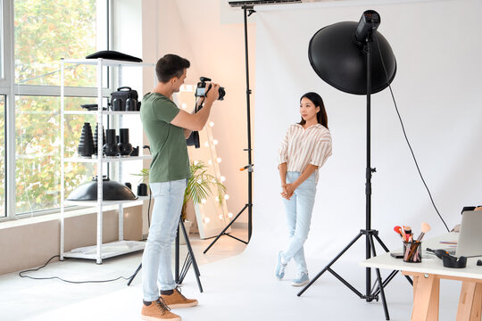 Male photographer taking picture of young Asian woman in studio