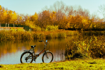 Fototapeta premium A bicycle without a person stands on the shore of a forest lake in autumn