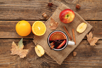 Cup of hot mulled wine with apple and orange on wooden background