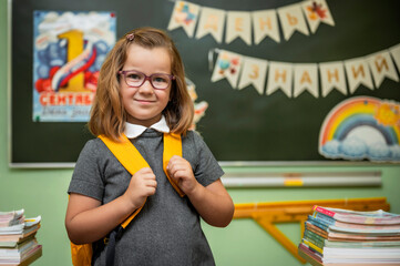 cute smiling girl 6 years old at school in the classroom looks at the camera, the theme is back to school