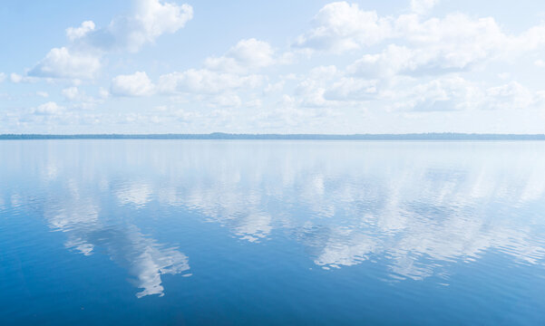 natural landscape, waterscape with large water body under a blue sky with clouds and a distant wooded shore