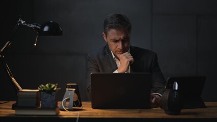 Businessman sitting at desk with laptop computer. Entrepreneur working in office, thinking. Older,...
