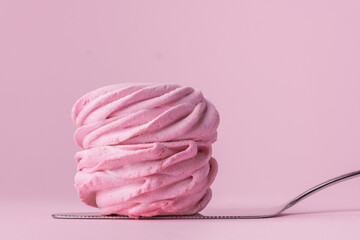 Macro shot of single pink berry homemade marshmallow on confectionery spatula. Zefir dessert with red currant mousse on the pink pastel background.