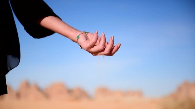 Saudi Arabia desert with hand holding sand that is falling with dark clothing and jewelry