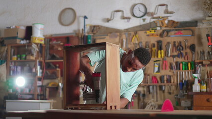 One concentrated black carpenter using drilling equipment at carpentry workshop