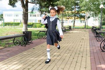 Cheerful funny girl with toothless smile in school uniform with white bows running in school yard....