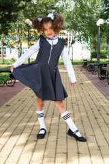 Cheerful funny girl with a toothless smile in a school uniform with white bows in school yard. Back...