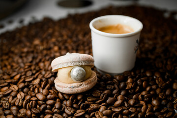 Appetizing view on white cup with coffee and macaroon on top of fresh roasted coffee beans