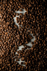Freshly roasted coffee beans with logo silohuette on white surface, top view. Coffee beans background