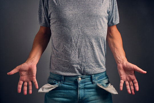 Man in gray crumpled T shirt and jeans with turned out, empty pockets.Concept of bankruptcy and poverty.