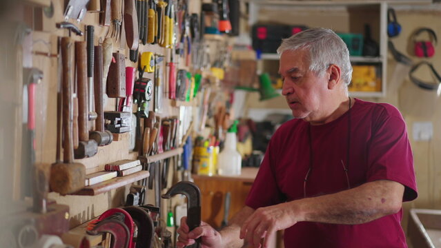 Senior man organizing tools hanging on wall at workshop carpentry shop
