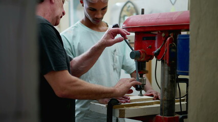 Senior staff guiding carpentry apprentice to use machine at workshop. Candid scene of people working in industrial job, diverse workers