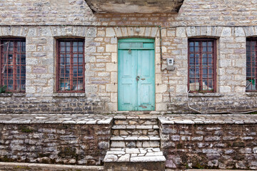 Fototapeta na wymiar Old municipal stone building with bright green door and windows with iron bars, used as a warehouse in Fragkista village, in the mountainous Evritania region, Central Greece, Greece, Europe.