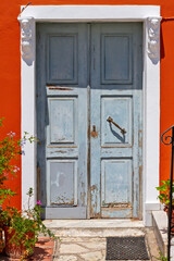 Traditional wooden door entrance with double doors, a stone built lintel and threshold, and a bright red wall, in Parga, Preveza, Greece