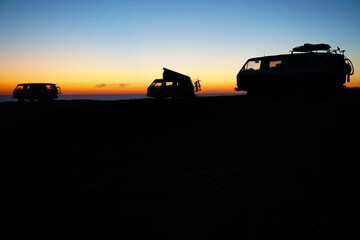 Fototapeta premium silhouette of camper vans parking on cliff during sunset 