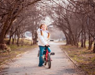 Obraz premium smiling happy little girl standing close to the bike in the spring
