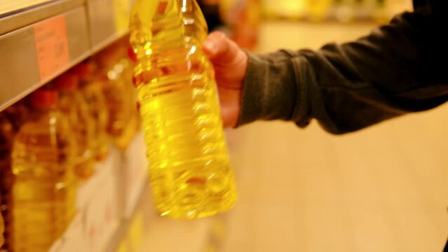male hand holds sunflower oil on blurred background, row of shelves with groceries in supermarket, concept of marketing, prices for consumer goods, consumer basket, rising prices for essential goods