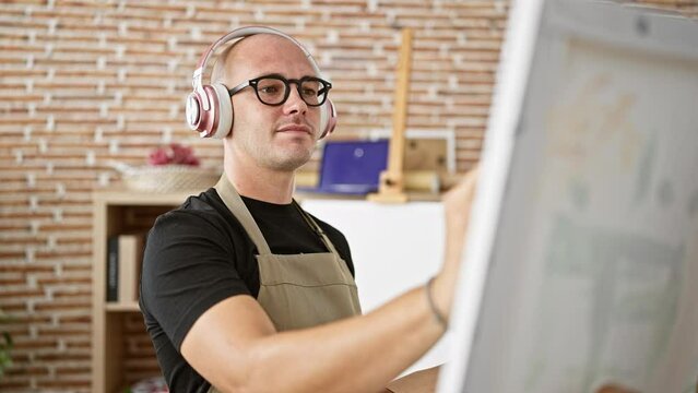 Young hispanic man artist listening to music drawing at art studio