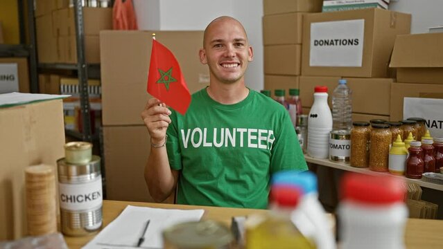 Young hispanic man volunteer smiling confident holding morocco flag at charity center