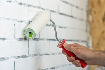 A worker paints a brick wall with white paint using a paint roller