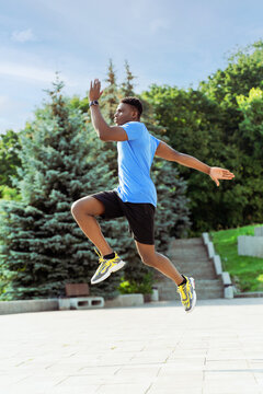 African american man runner jumping at green street while enjoying sport