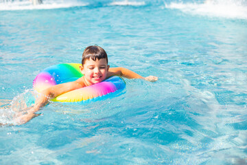 Cute baby boy swims with a rainbow inflatable ring in a clean pool