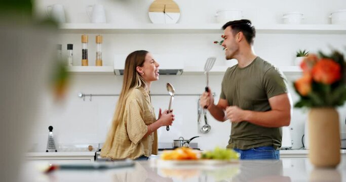 Dancing, utensils and couple singing in the kitchen for bonding, having fun or happiness. Smile, music and young man and woman doing karaoke together to playlist, radio or album at a modern apartment