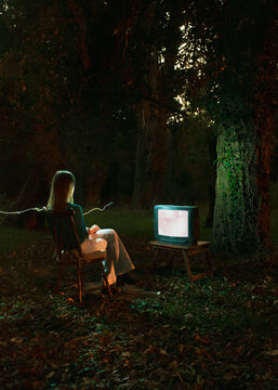 Persona mujer sentada frente a un televisor en medio de un bosque de noche