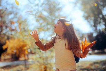 Happy Playful Kid Enjoying Playing with Foliage Outdoors. Little girl feeling cheerful going back to school
