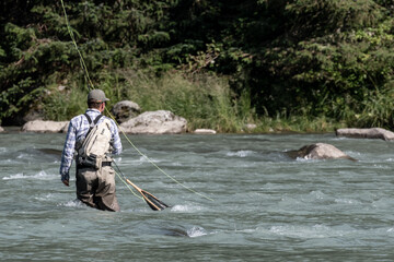 Fly fisherman fishing in the middle of the river on a summer day.