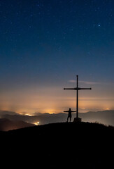 person open arms cross on a mountain at night with lights and stars