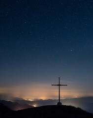 cross on a mountain at night with lights and stars