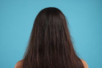 Woman with damaged messy hair on light blue background, back view