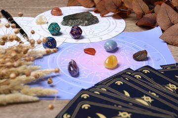 Zodiac wheel, tarot cards, astrology dices and gemstones on wooden table, closeup