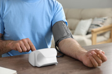Man measuring blood pressure at table indoors, closeup