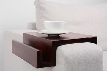 Cup of coffee on sofa with wooden armrest table indoors. Interior element