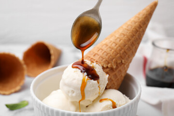 Pouring caramel sauce onto ice cream on table, closeup