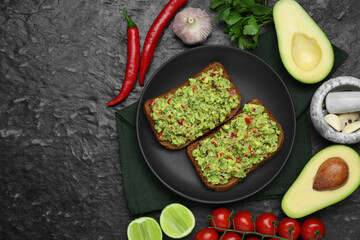 Slices of bread with tasty guacamole and ingredients on black textured table, flat lay. Space for text