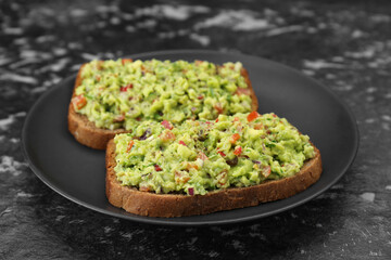 Slices of bread with tasty guacamole on black textured table, closeup