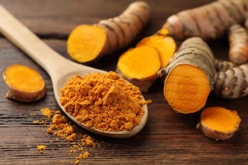 Aromatic turmeric powder and raw roots on wooden table, closeup