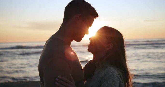 Sunset, beach and couple hug, kiss and share moment at the ocean for bond, freedom or travel. Sunrise, love and silhouette of man with woman embrace at sea with lens flare, care or romance in nature
