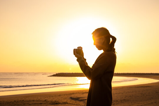 Lady silhouette with using camera to take photo at seaside beach