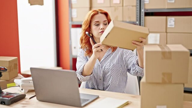 Young redhead woman ecommerce business worker scanning packages using smartphone at office