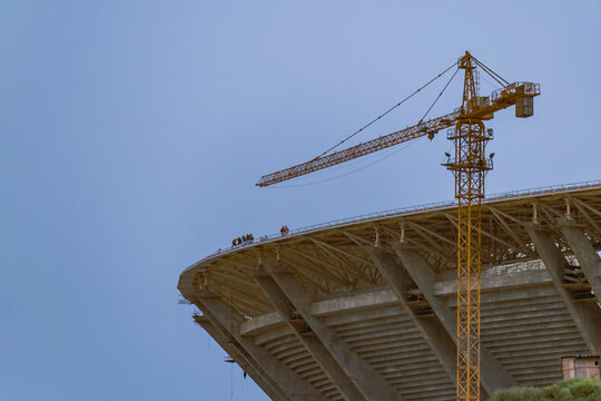 The new home soccer stadium of Mouloudia Club d'Alger in Douera, Algiers under construction. Low angle view with a big crane and unrecognizable workers on the top roof afar. 