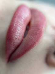 permanent makeup on the lips of a young woman of a delicate peach shade close-up, a girl after a cosmetic procedure with smooth and clean healthy skin.