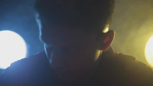 Film-like dolly shot of a man in a red shirt sitting on a table preparing for a stealth mission packing his weapons and knives with creative dramatic lighting technique, HD - 24 fps - Prores